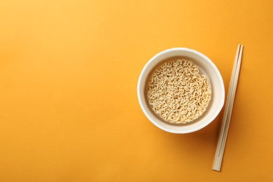 Photo of Cup of instant noodles with chopsticks on color background, top view. Space for text