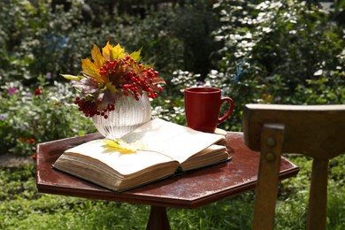 Photo of Cup of hot drink, book and dry leaves with viburnum on wooden table outdoors. Autumn atmosphere
