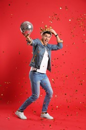 Happy man in party crown with disco ball and confetti on red background