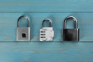 Different padlocks on light blue wooden table, flat lay