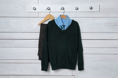Shirt, jumper and pants hanging on white wooden wall. School uniform
