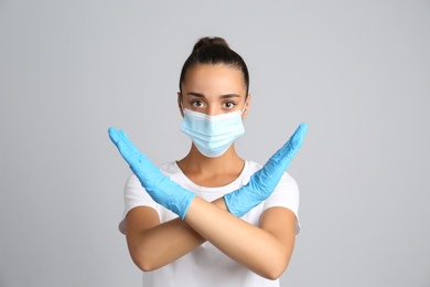Woman in protective mask showing stop gesture on grey background. Prevent spreading of COVID‑19
