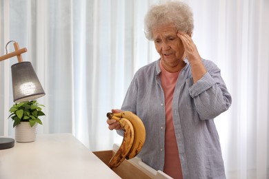 Senior woman finding bananas in chest of drawers at home. Age-related memory impairment