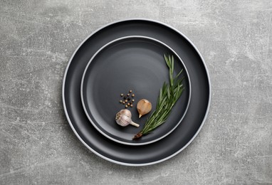 New dark plates with rosemary, garlic and peppercorns on light grey table, top view