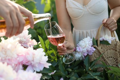 Photo of Women with bottle and glass of rose wine in peony garden, closeup