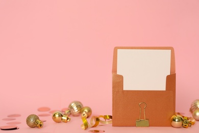 Blank greeting card in envelope and Christmas balls on pink background, space for text