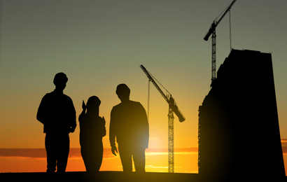 Silhouettes of engineers near construction site at sunrise