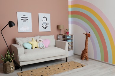 Cute child's room interior with sofa, toys and rainbow art on wall