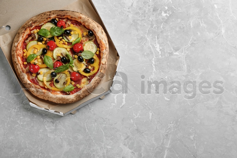 Photo of Tasty vegetable pizza in cardboard box on light grey table, top view. Space for text