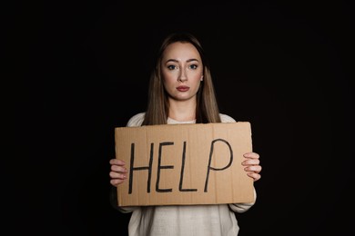 Unhappy young woman with HELP sign on dark background
