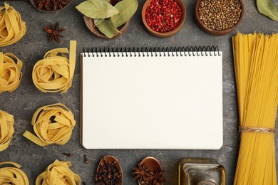 Blank recipe book, spices and raw pasta on dark grey table, flat lay. Space for text