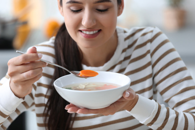 Young woman eating tasty vegetable soup indoors
