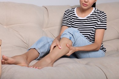 Young woman rubbing sore leg on sofa, closeup