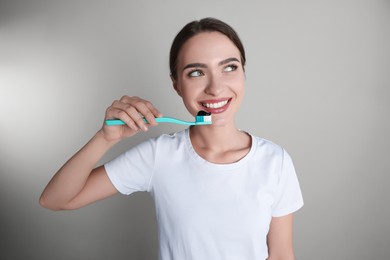 Young woman holding toothbrush with charcoal toothpaste on grey background
