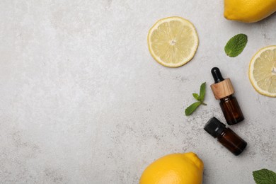 Bottles of citrus essential oil and fresh lemons on light table, flat lay. Space for text
