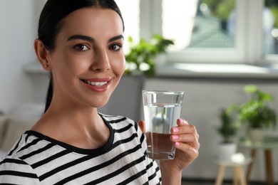 Young woman with glass of water indoors, closeup. Refreshing drink