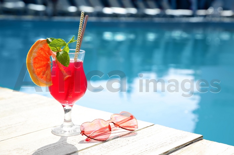 Refreshing cocktail and sunglasses near outdoor swimming pool on sunny day. Space for text