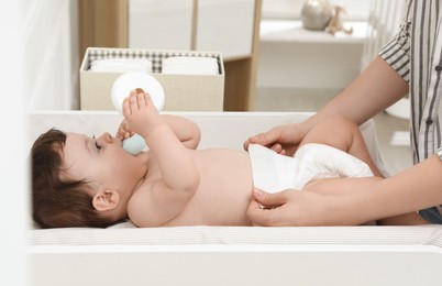 Photo of Mother changing baby's diaper on table at home, closeup