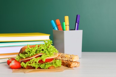 Photo of Tasty healthy food and different stationery on white wooden table near green chalkboard, space for text. School lunch