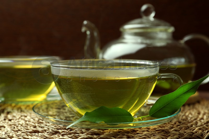 Photo of Fresh green tea in glass cups, leaves and teapot on table, closeup