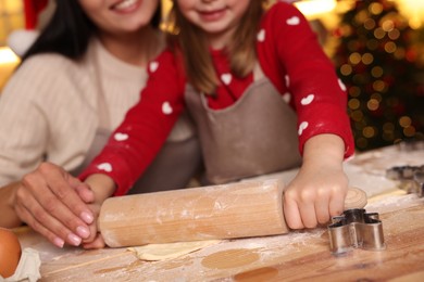 Photo of Mother and her daughter making delicious Christmas cookies at wooden table indoors, closeup