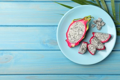 Plate with delicious cut white pitahaya fruit and palm leaf on light blue wooden table, flat lay. Space for text