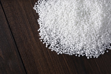 Pellets of ammonium nitrate on wooden table, flat lay with space for text. Mineral fertilizer