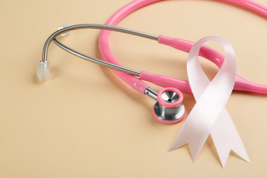 Photo of Pink ribbon and stethoscope on beige background, closeup. Breast cancer concept