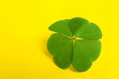 Beautiful green four leaf clover on yellow background, closeup. Space for text