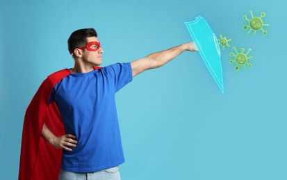 Man wearing superhero costume fighting against viruses on light blue background