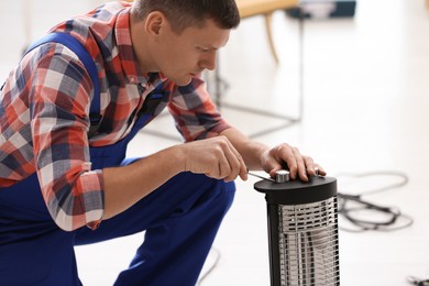 Professional technician repairing electric halogen heater with screwdriver indoors