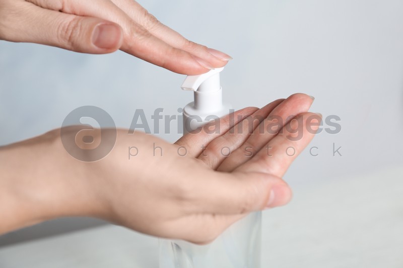 Woman applying antiseptic gel on hand against light background, closeup