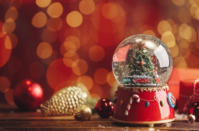 Beautiful snow globe with Christmas tree on wooden table against blurred festive lights. Space for text