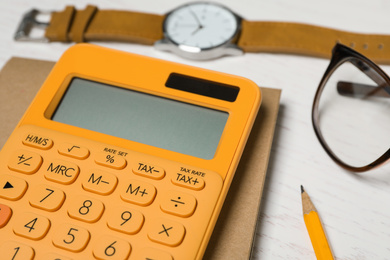 Calculator, notebook, watch and glasses on white wooden table, closeup. Tax accounting