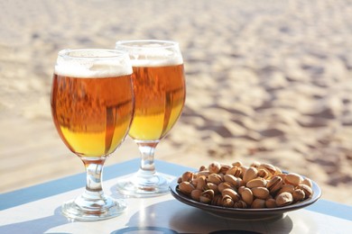 Photo of Glasses of cold beer and pistachios on table outdoors