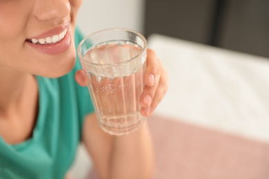 Young woman drinking pure water from glass indoors, closeup. Space for text