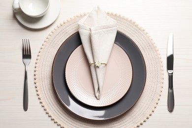 Photo of Plates with fabric napkin, decorative ring and cutlery on white wooden table, flat lay