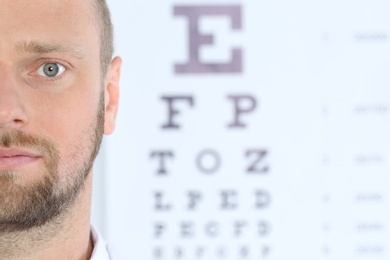 Closeup view of man and blurred eye chart on background. Space for text