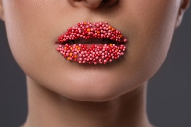 Young woman with beautiful lips covered confectionery sprinkles on gray background, closeup