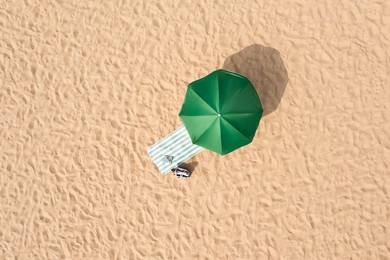 Beach umbrella near towel and other vacationist's stuff on sand, aerial view