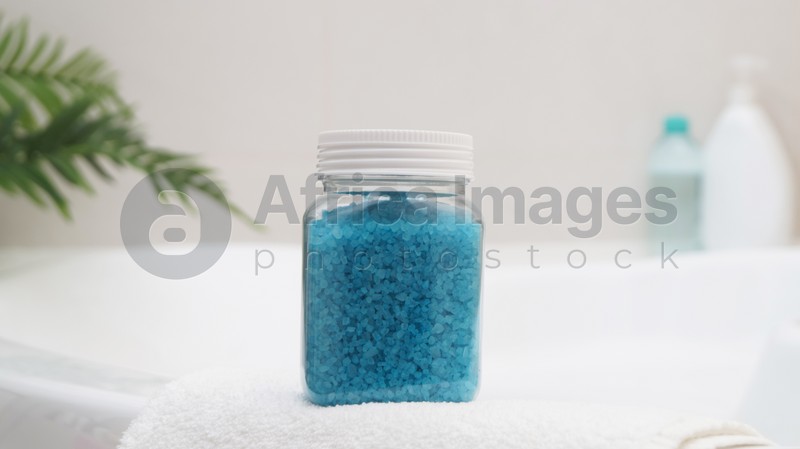 Jar with sea salt and fluffy towel on bath