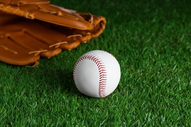 Photo of Catcher's mitt and baseball ball on green grass. Sports game