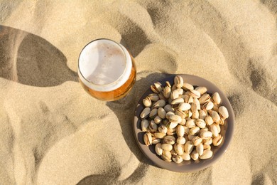 Glass of cold beer and pistachios on sandy beach, flat lay