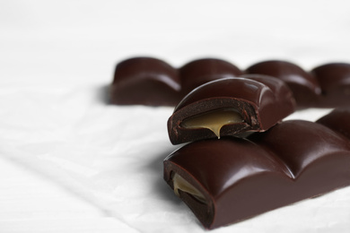 Pieces of chocolate with caramel filling on white table, closeup. Space for text