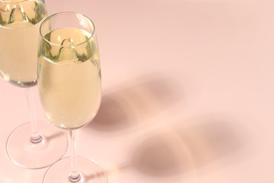 Photo of Glasses of delicious sparkling wine on pale pink background, closeup. Space for text