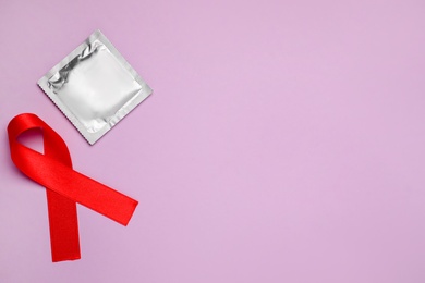 Red ribbon and condom on violet background, flat lay with space for text. AIDS disease awareness