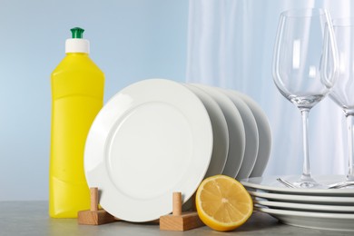 Photo of Glasses, clean dishware and bottle of detergent on grey marble table