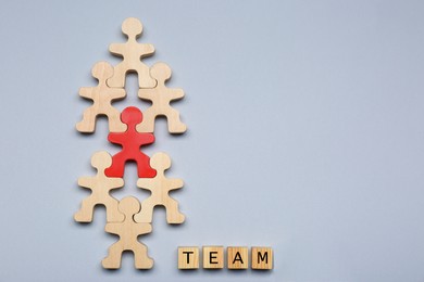 Photo of Red figure among wooden ones and cubes with word Team on light grey background, flat lay with space for text. Recruiter searching employee