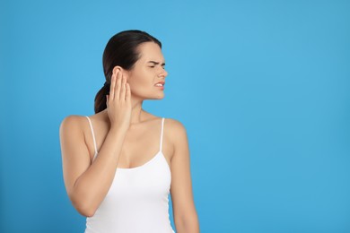 Photo of Young woman suffering from ear pain on light blue background, space for text