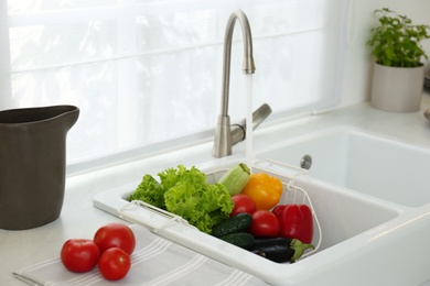 Photo of Many fresh ripe vegetables under tap water in kitchen sink